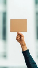 A hand holds a blank cardboard sign against a blurred background, symbolizing communication or expression.