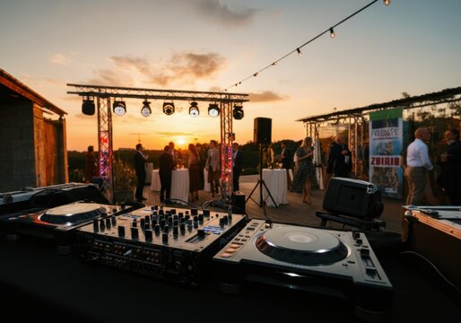 Professional dj equipment set up on a rooftop at sunset, with blurred guests enjoying a corporate event party in the background