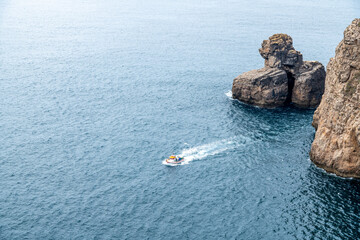 Motorboat on deep blue sea passing rugged coastal cliffs