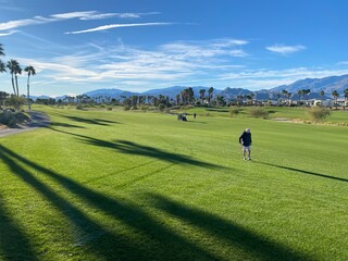 A senior man on the fairway about to hit a golf ball on a beautiful day in Palm Springs, California, USA, on a beautiful sunny winter day with the mountains in the background.
