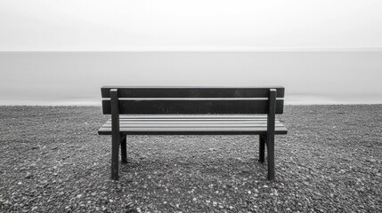 Lonely bench on a pebble beach, overlooking a calm sea on a misty day.