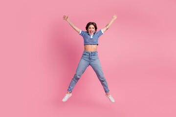Joyful young woman in casual striped t-shirt and jeans leaping with excitement against a vibrant pink background
