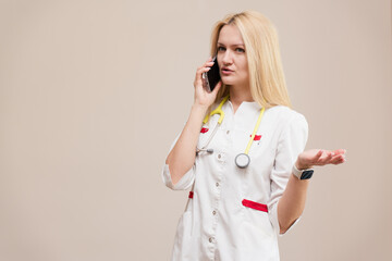 A professional female doctor in a white coat with a stethoscope around her neck, talking on the...