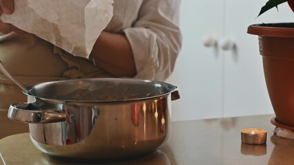 Person preparing dough in kitchen with candle and plant nearby