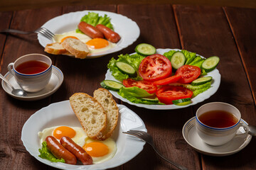 Breakfast two plates of scrambled eggs with chanterelles and white bread, tomato salad and tea in cups