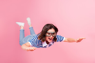 Joyful young woman with trendy bob hair and goggles simulates flying against a vibrant pink...
