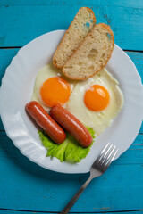 Breakfast fried eggs with sausages, crispy white bread, on a blue table