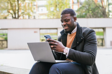 Young african entrepreneur managing business using laptop and smartphone outdoors