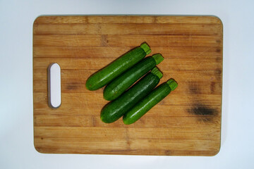Four baby marrow on a brown wooden cutting board.