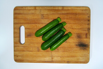 Four baby marrow on a brown wooden cutting board.