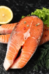 Fresh raw salmon steaks with spices, lemon, lettuce and dill on dark textured table, closeup