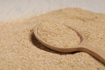 Pile of oat bran and wooden spoon on table, closeup