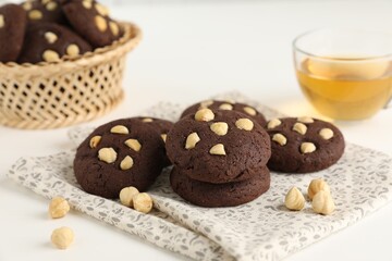 Tasty chocolate cookies with hazelnuts and tea on white table, closeup
