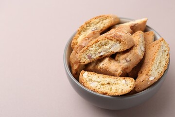 Tasty almond biscuits (Cantuccini) in bowl on beige background, closeup. Space for text