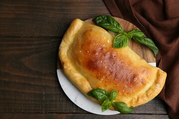 Tasty vegetarian calzone with basil on wooden table, top view. Space for text
