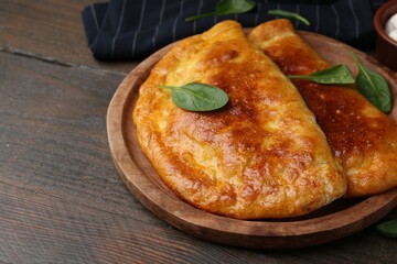 Tasty calzones with basil on wooden table, closeup. Space for text