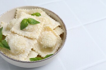 Delicious ravioli with cheese and basil on white tiled table, closeup. Space for text