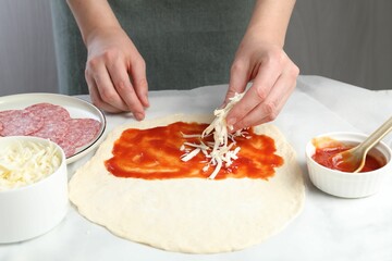 Making calzone pizza. Woman putting cheese onto dough with sauce at table, closeup