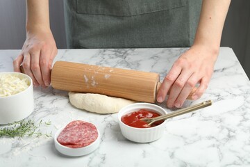 Making calzone pizza. Woman shaping dough with rolling pin at white marble table, closeup
