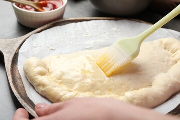 Woman brushing egg yolk on calzone pizza at grey table, closeup