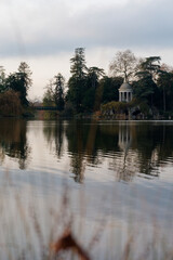 Obraz premium View of the rotunda and artificial grotto reflecting on the calm waters of Lake Daumesnil in Bois de Vincennes, surrounded by lush greenery