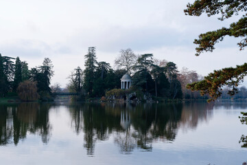 Obraz premium Scenic view of the rotunda and artificial grotto on Ile de Reuilly at Lake Daumesnil in the serene Bois de Vincennes during a tranquil afternoon