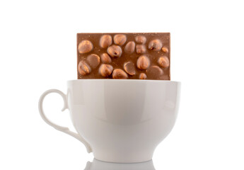 One bar of dark chocolate with hazelnuts in a ceramic dish, close-up, isolated on a white background.