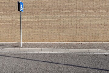 Yellow brick wall at the roadside with a pedestrian crossing sign on the left. Sidewalk and asphalt...