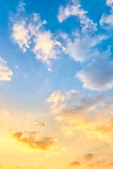A bright sky at sunrise or sunset, with soft gradients of blue mixed with gold and orange, as clouds spread out, some illuminated by sunlight.