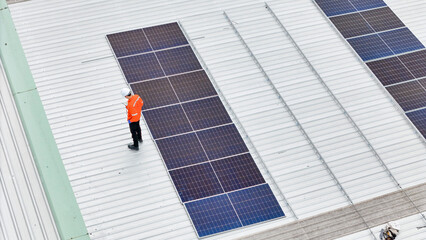 technician in safety gear inspects solar panels on a metal rooftop, holding a tool. The scene emphasizes renewable energy, solar technology, and maintenance of sustainable infrastructure.