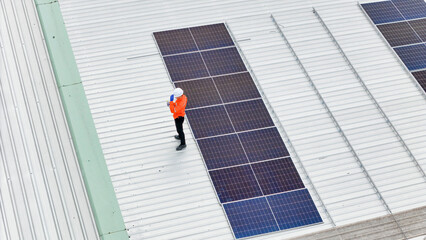 technician in safety gear inspects solar panels on a metal rooftop, holding a tool. The scene...