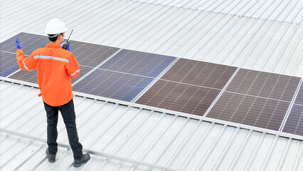 technician in hard hat and safety gear inspects solar panels on a metal rooftop, holding a tool. The scene emphasizes renewable energy, solar technology, and maintenance of sustainable infrastructure.