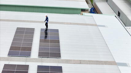technician in hard hat and safety gear inspects solar panels on a metal rooftop, holding a tool....