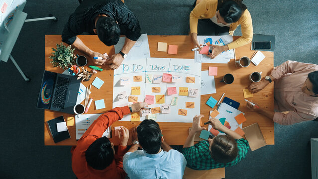 Top down aerial view of business team making scrum task board at meeting room. Group of people writing at paper and sticky notes for making kanban board to manage work flow. Top view. Convocation.