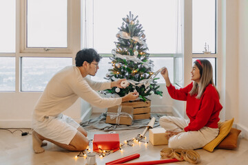 Asian husband and wife couple lover decorating Christmas tree together while the man helping woman packing decoration boxes.