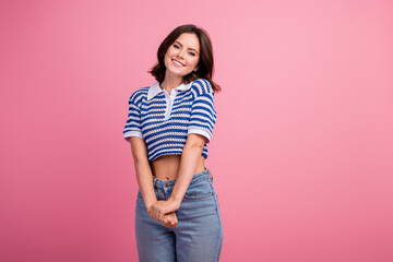 Charming young woman in stylish striped polo poses with a happy smile against a pink background, displaying her casual summer fashion