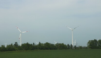 Fototapeta premium wind generators among green fields and groves, a combination of modern technologies, green energy and natural resources