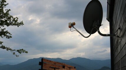 silhouette of satellite dish hanging on wooden wall of house or cottage against beautiful cloudy...