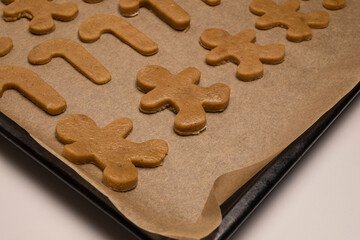 Festive New Year's Eve gingerbread men and gingerbread-shaped candies are on parchment paper on a baking tray, ready to go in the oven.