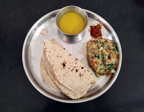 Indian spicy food served in a steel round plate with baigan ka bharta and wheat roti 