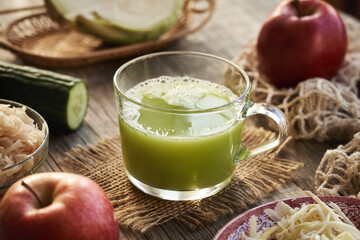 A cup of green cabbage juice with cucumber and red apples