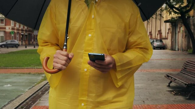 Using phone taxi app during rain, Unrecognizable man standing on the city streets under umbrella and using cellphone