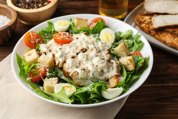 Tasty Caesar salad with chicken and tomatoes in bowl on wooden table, closeup