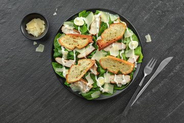 Delicious Caesar salad with chicken and cheese on black textured table, flat lay