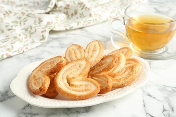 Delicious palmier cookies with tea on white marble table, closeup