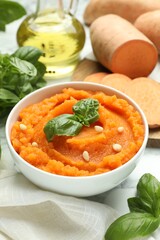 Tasty mashed sweet potato with basil, seeds in bowl and ingredients on table, closeup