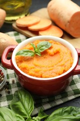 Tasty mashed sweet potato with basil in pot and fresh vegetables on table, closeup