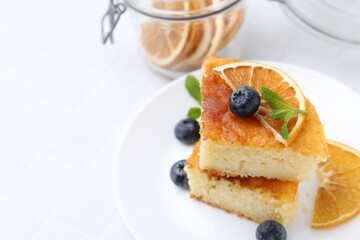Pieces of delicious semolina cake with blueberries and orange slices on white table, closeup. Space for text