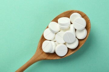 Antibiotic pills in spoon on turquoise background, top view