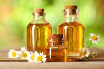 Bottles of essential oil and chamomile flowers on wooden table, closeup